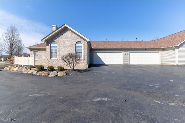 ranch-style house with aphalt driveway, a garage, brick siding, fence, and a chimney