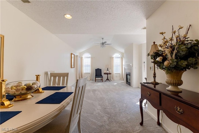 dining space with lofted ceiling, light colored carpet, ceiling fan, a textured ceiling, and a tile fireplace