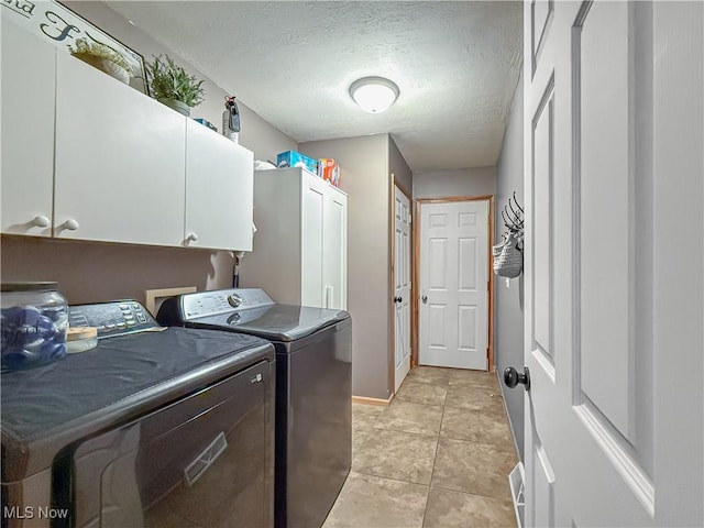 laundry room featuring a textured ceiling, light tile patterned flooring, separate washer and dryer, baseboards, and cabinet space