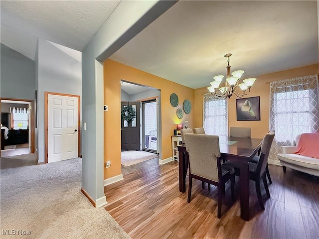 dining space featuring baseboards, vaulted ceiling, a notable chandelier, and wood finished floors