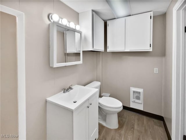 half bathroom with toilet, wood finished floors, vanity, and heating unit