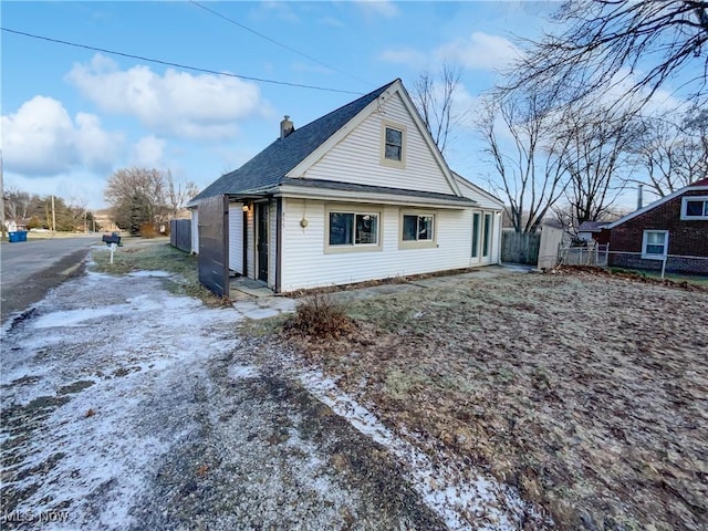 snow covered property with roof with shingles, a chimney, and fence