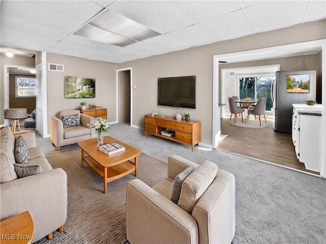 living area featuring carpet floors, a drop ceiling, visible vents, and baseboards