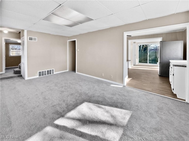 carpeted empty room featuring a paneled ceiling, visible vents, and baseboards