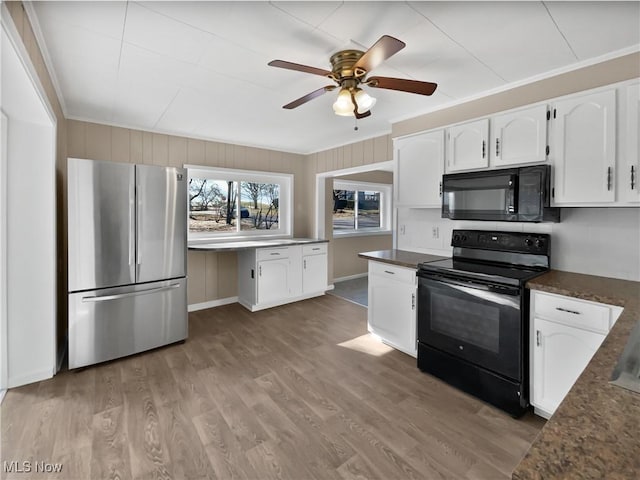 kitchen with dark countertops, black appliances, white cabinets, and wood finished floors