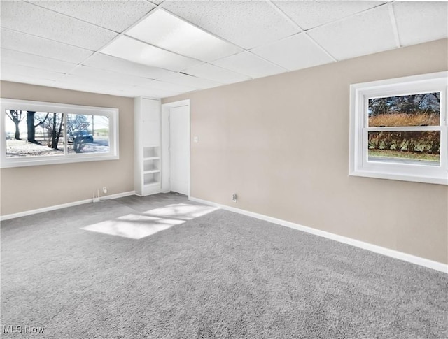 carpeted empty room with baseboards and a drop ceiling