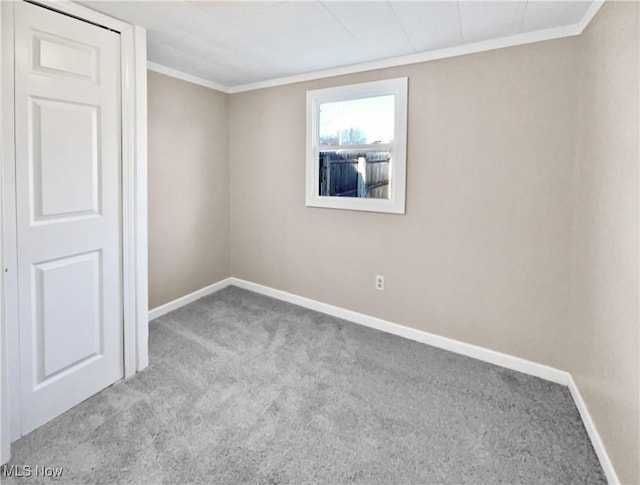 carpeted empty room featuring crown molding and baseboards