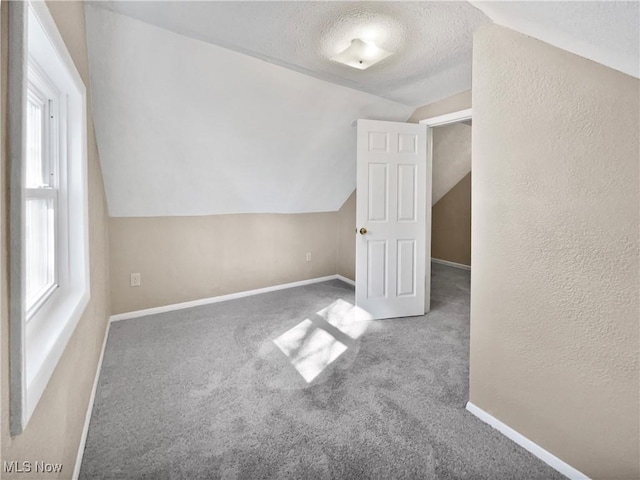 additional living space with carpet flooring, vaulted ceiling, a textured ceiling, and baseboards