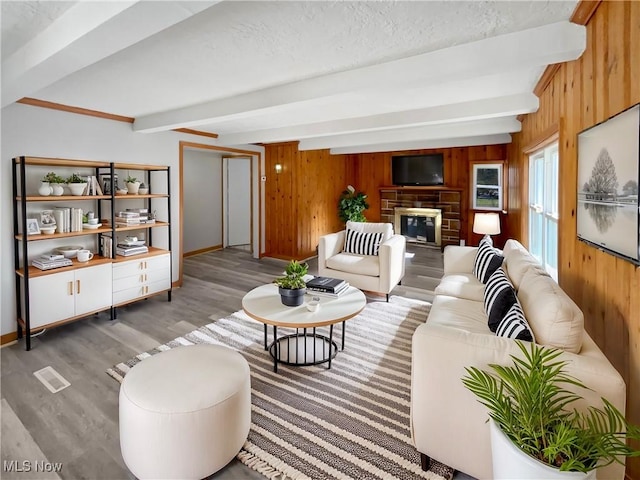 living area with beamed ceiling, a glass covered fireplace, wood walls, and wood finished floors