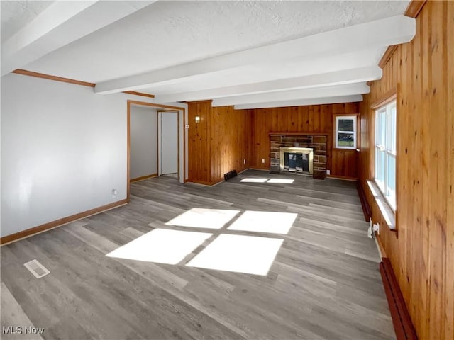 unfurnished living room featuring beam ceiling, wooden walls, and a stone fireplace
