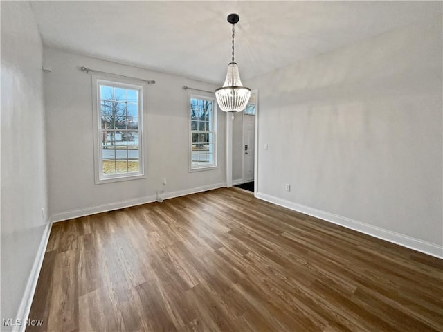 unfurnished dining area with a chandelier, dark wood-type flooring, and baseboards