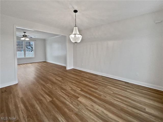 unfurnished dining area featuring dark wood-style flooring, baseboards, and ceiling fan with notable chandelier