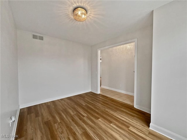 spare room with wood finished floors, visible vents, and baseboards