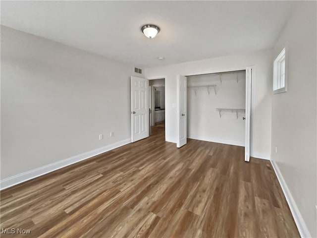 unfurnished bedroom featuring a closet, wood finished floors, visible vents, and baseboards