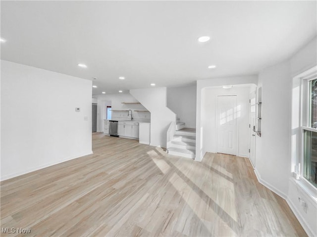 unfurnished living room featuring recessed lighting, stairway, light wood-style floors, a sink, and baseboards