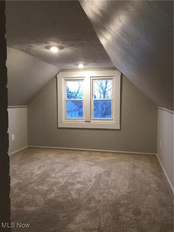 bonus room featuring a textured ceiling, carpet, lofted ceiling, and baseboards