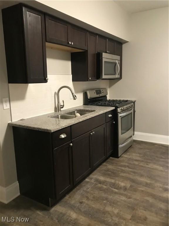 kitchen with baseboards, appliances with stainless steel finishes, dark wood-type flooring, light stone countertops, and a sink