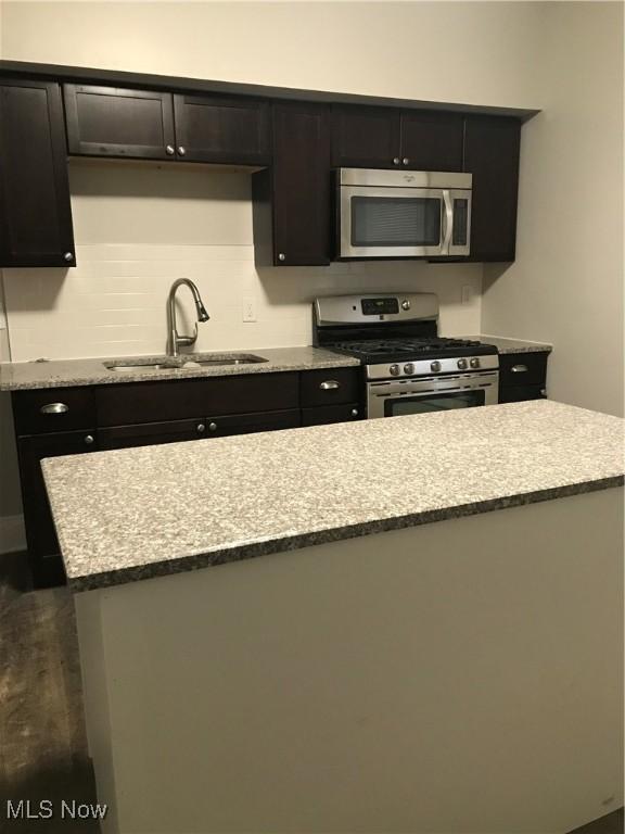 kitchen with light stone counters, stainless steel appliances, dark wood-type flooring, a sink, and tasteful backsplash