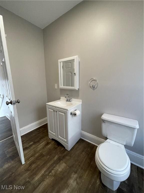 half bathroom with vanity, wood finished floors, toilet, and baseboards