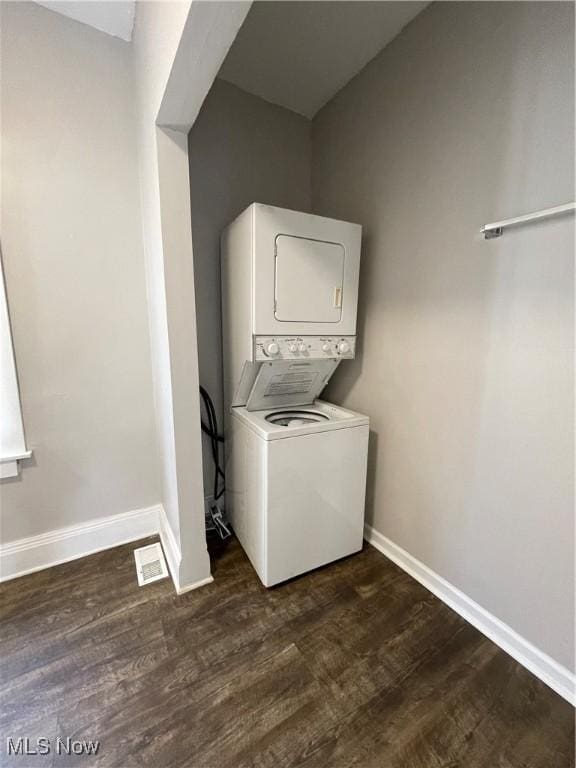 washroom featuring stacked washer and clothes dryer, dark wood-style flooring, visible vents, laundry area, and baseboards