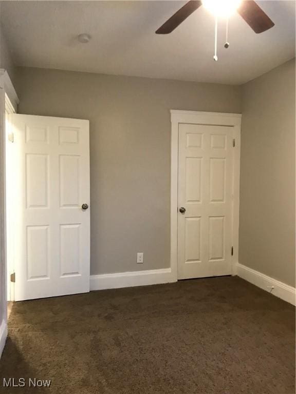 unfurnished bedroom with baseboards, dark carpet, and ceiling fan