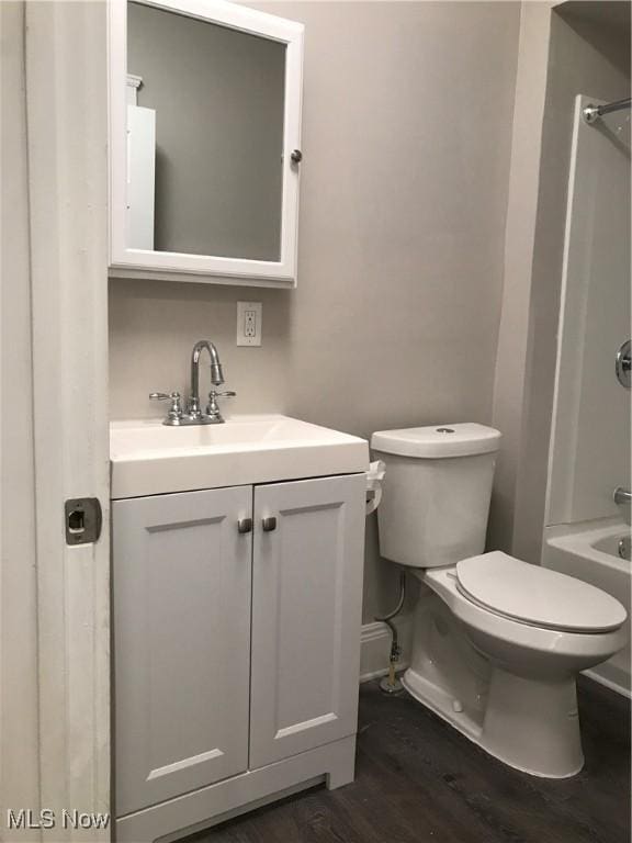 bathroom with shower / tub combination, toilet, wood finished floors, vanity, and baseboards