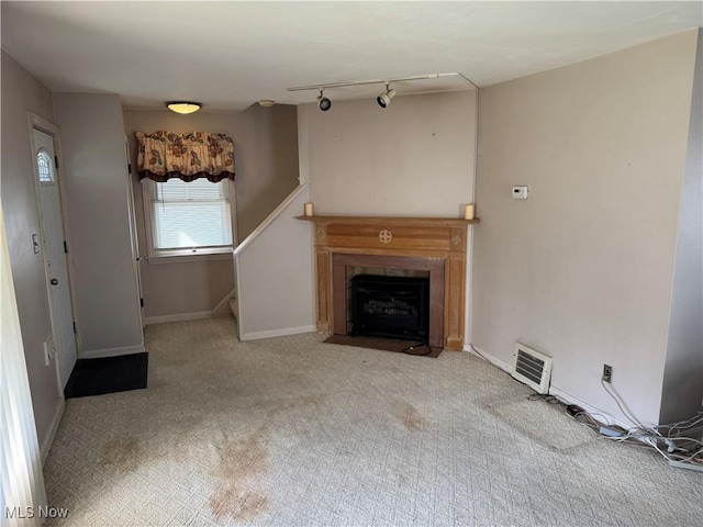 unfurnished living room with visible vents, baseboards, a fireplace with flush hearth, stairway, and rail lighting