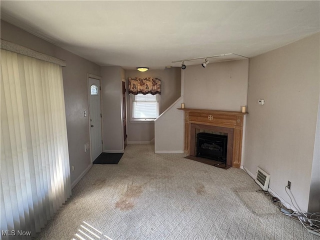 unfurnished living room featuring rail lighting, a fireplace with flush hearth, visible vents, and baseboards