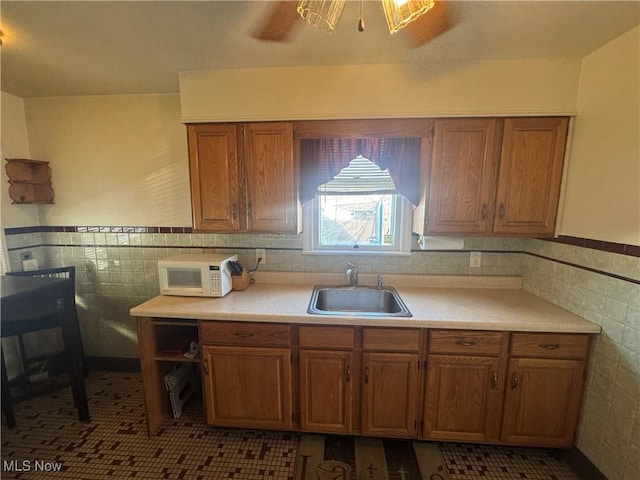 kitchen with white microwave, a sink, tile walls, light countertops, and brown cabinets