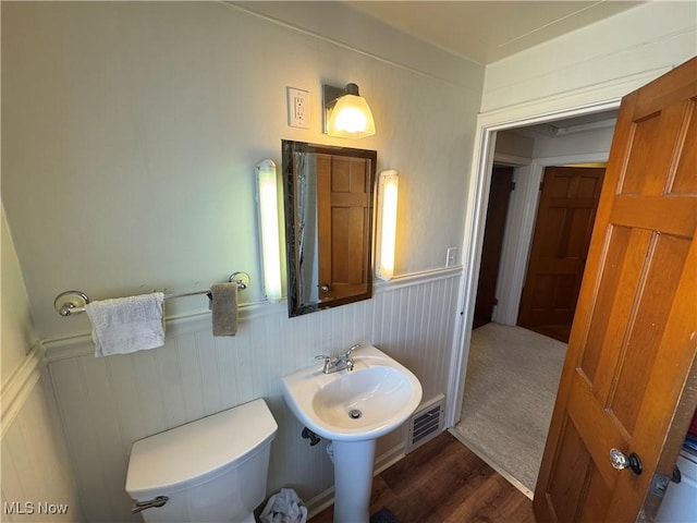 bathroom with a wainscoted wall, visible vents, toilet, and wood finished floors