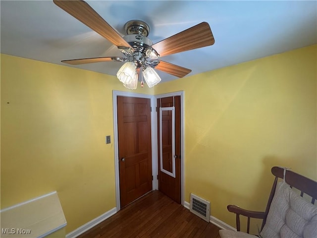 interior space with dark wood-type flooring, a ceiling fan, visible vents, and baseboards