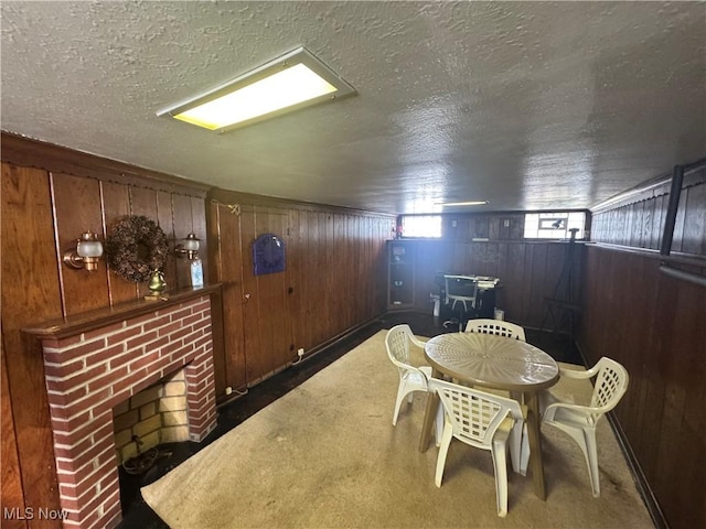 dining space with carpet, a textured ceiling, a brick fireplace, and wooden walls