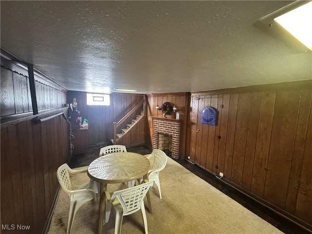 dining room featuring wooden walls, stairs, a textured ceiling, carpet floors, and a fireplace