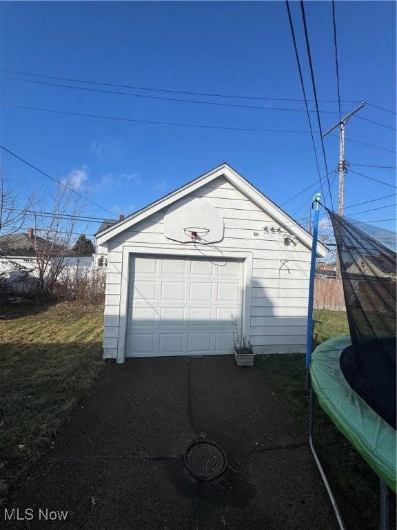 detached garage featuring driveway and a trampoline