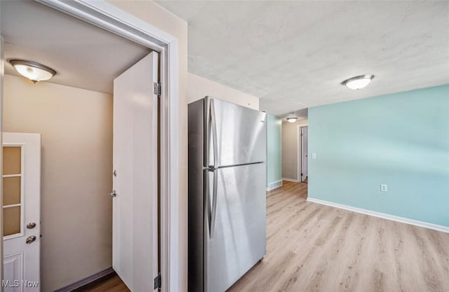 kitchen featuring light wood finished floors, baseboards, and freestanding refrigerator