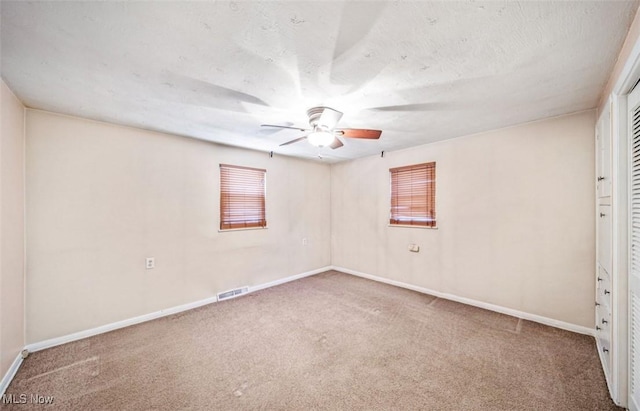 carpeted spare room featuring a ceiling fan, visible vents, baseboards, and a textured ceiling