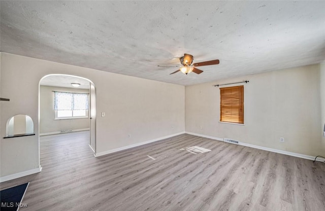 unfurnished room with arched walkways, wood finished floors, visible vents, and baseboards