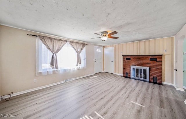 unfurnished living room with visible vents, baseboards, a ceiling fan, wood finished floors, and a brick fireplace