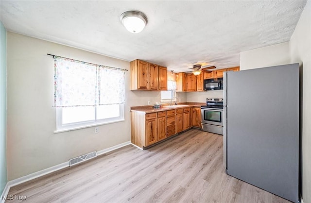 kitchen with stainless steel appliances, a sink, visible vents, baseboards, and light wood-type flooring