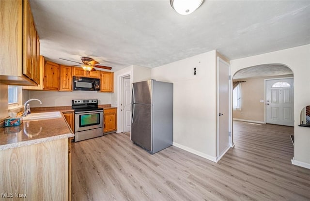 kitchen featuring arched walkways, light wood finished floors, appliances with stainless steel finishes, a sink, and baseboards