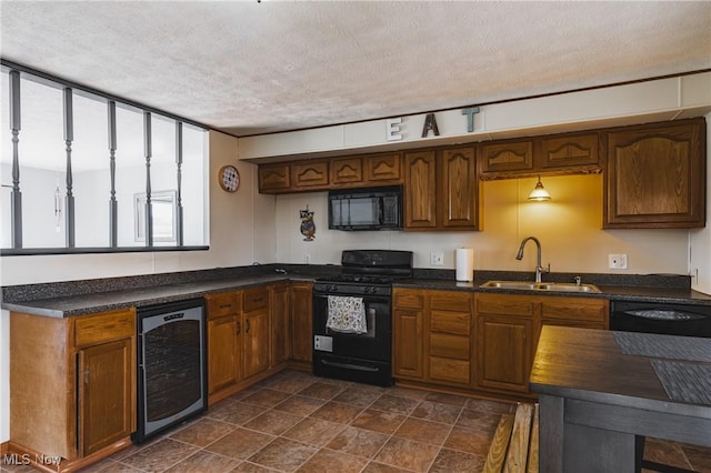 kitchen featuring brown cabinetry, wine cooler, a textured ceiling, black appliances, and a sink