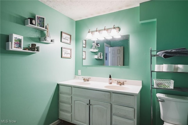 bathroom featuring double vanity, a textured ceiling, toilet, and a sink