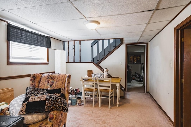 carpeted dining area with a paneled ceiling, baseboards, and stairs