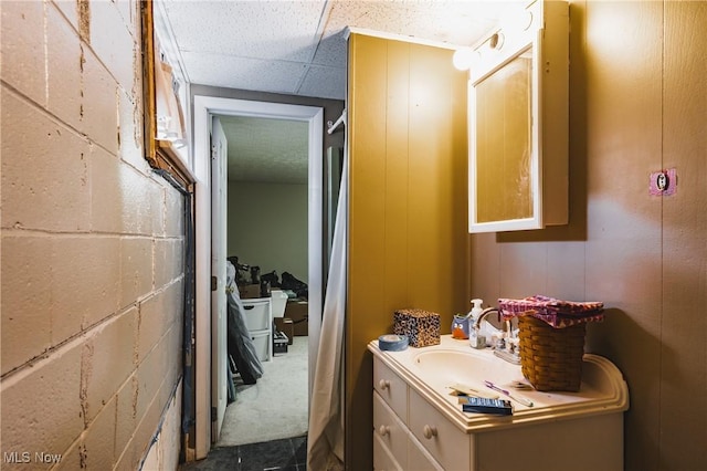 bathroom featuring concrete block wall, a drop ceiling, and vanity