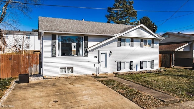 split foyer home with a shingled roof, a front yard, and fence