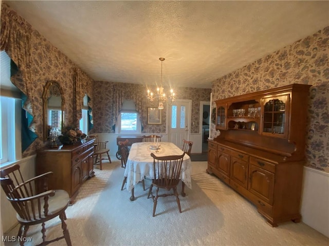 dining area with a wainscoted wall, a notable chandelier, light colored carpet, a textured ceiling, and wallpapered walls