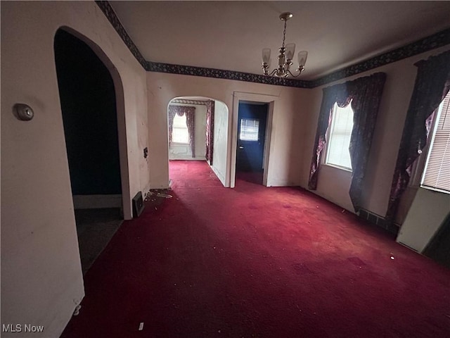 carpeted spare room with crown molding, arched walkways, and a notable chandelier