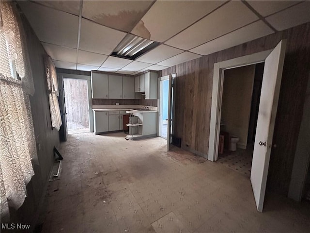 kitchen featuring a paneled ceiling, wooden walls, gray cabinets, and light countertops