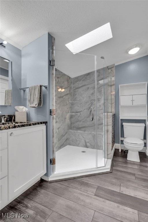 bathroom featuring toilet, a textured ceiling, vanity, a shower stall, and wood finish floors