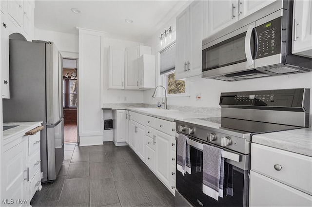 kitchen with stainless steel appliances, white cabinetry, a sink, and dark tile patterned floors